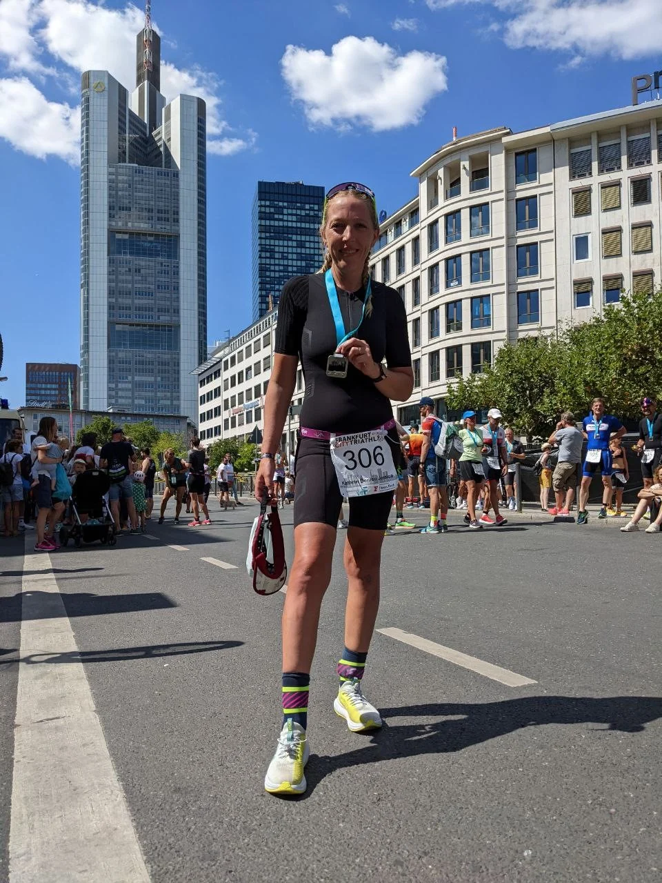 Läufer mit Medaille, Startnummer 306, Sportkleidung, Sonnenbrille, bunte Socken, Neonschuhe; Stadtstraße im Hintergrund mit Wolkenkratzern und Menschenmenge.