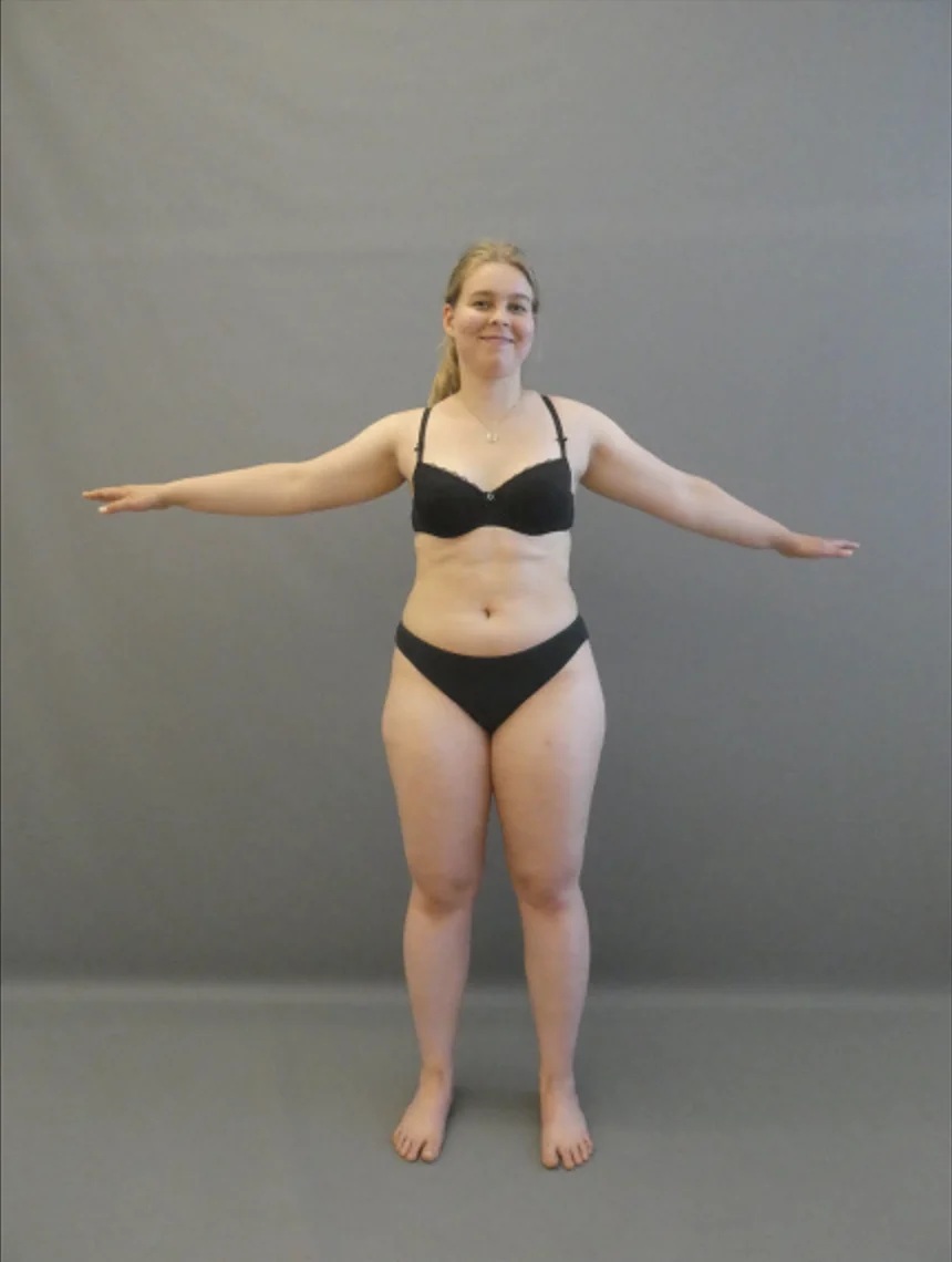 Person im schwarzen Bikini mit ausgestreckten Armen vor grauem Hintergrund.
