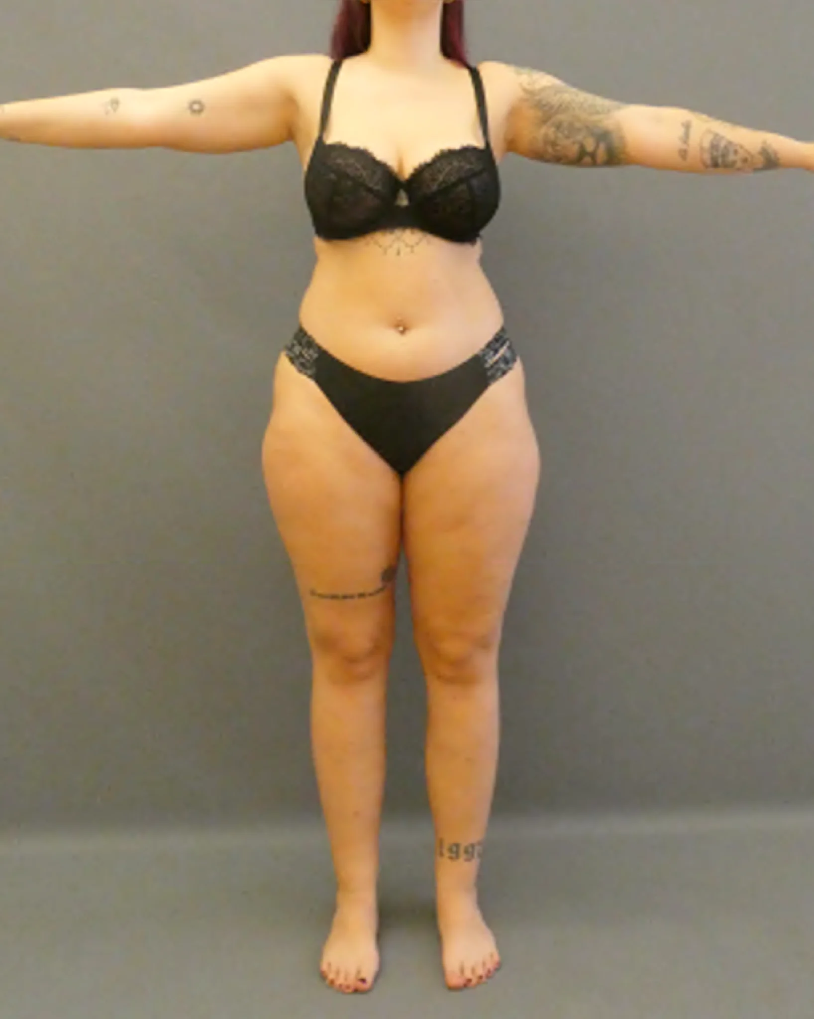 Person in schwarzer Unterwäsche mit Tattoos auf Armen und Beinen vor schlichtem grauem Hintergrund.